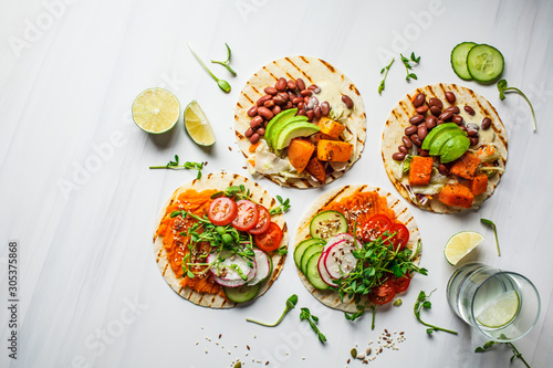 Open vegan tortilla wraps with sweet potato, beans, avocado, tomatoes, pumpkin and  sprouts on white background, flat lay, copy space. Healthy vegan food concept. photo