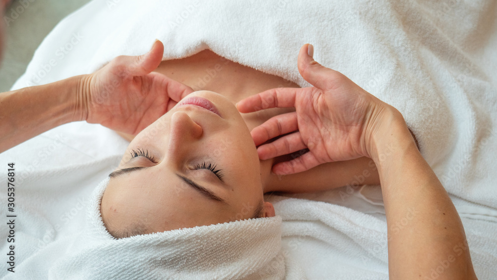 Close up portrait of a beautiful young smiling woman with a towel on her head is receiving a facial massage and spa treatment for perfect skin in a luxury wellness center. Close up portrait of a beautiful young smiling woman with a towel on her head is receiving a facial massage and spa treatment for perfect skin in a luxury wellness center.