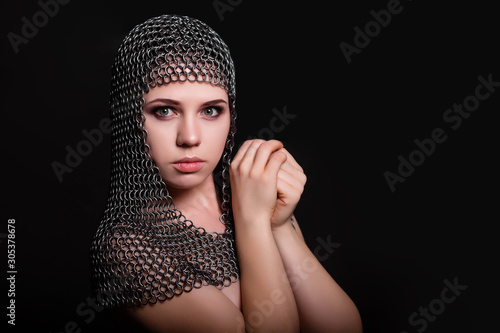 Portrait of a beautiful, young girl in a chainmail hood on a black background. Model with clean skin.