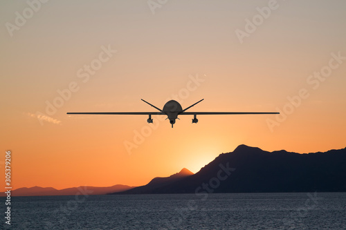 Silhouette of spy drone flying over the sea (UAV) and on the background beautiful view of sun hiding behind surface of mountain