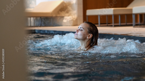An young female is enjoying and having relax in a whirlpool bath tube in a luxury wellness center.