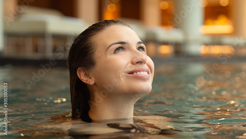 Portrait of an young smiling woman is enjoying and having relax in a indoor swimming pool in a luxury wellness center.