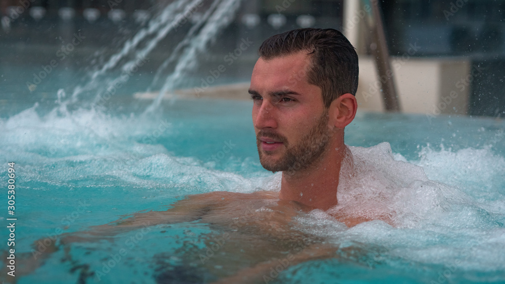 Portrait of an young man is enjoying and having relax in a whirlpool bath tube in a luxury wellness center.