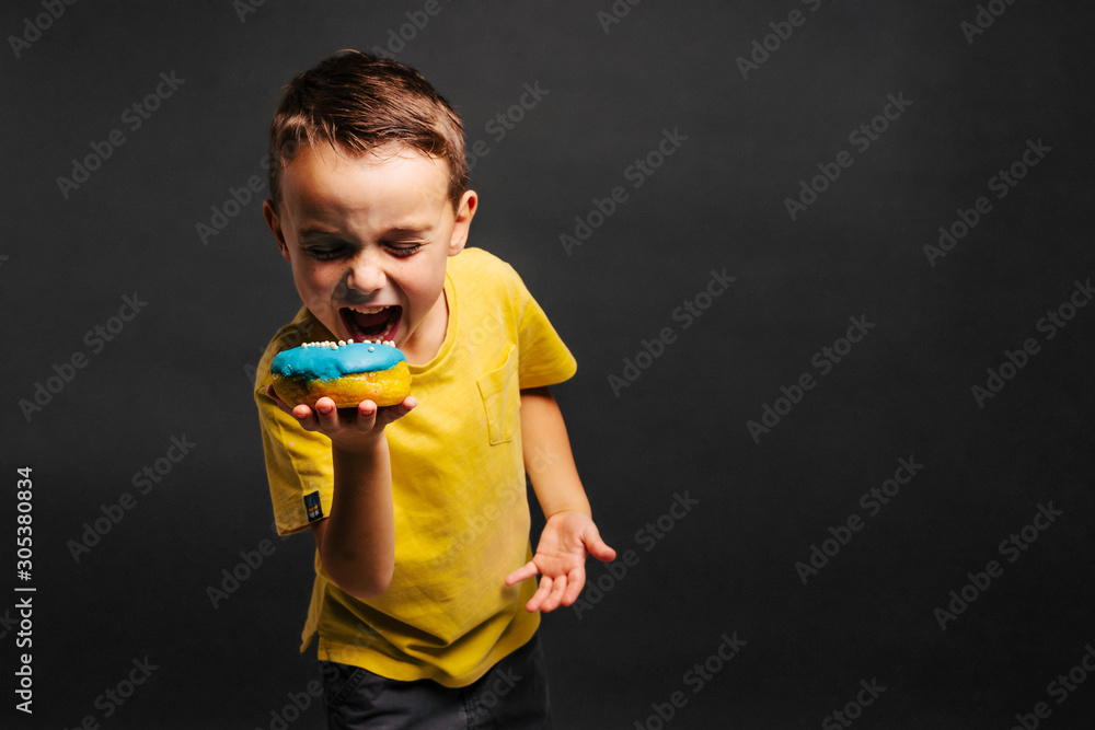 Happy cute boy is having fun played with donuts on black background wall. Happy cute boy is having fun played with donuts on black background wall.