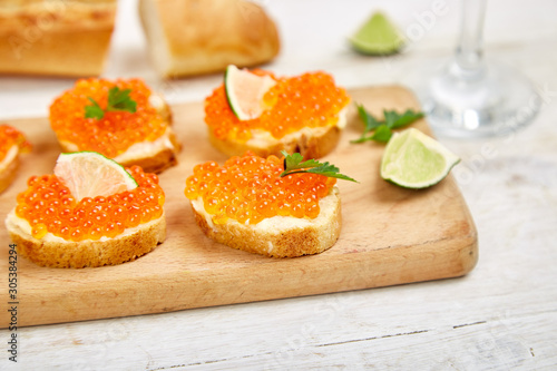 Salmon red caviar in bowl and Sandwiches with on wooden cutting board, glass with champagne on white background copy space.