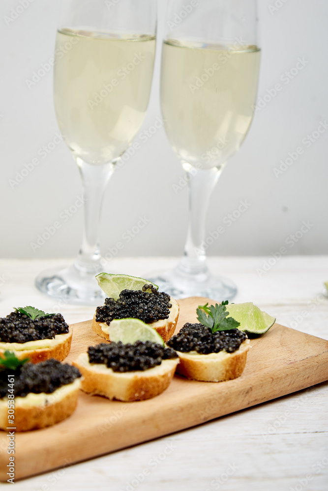 Sandwiches with black caviar. Sturgeon black caviar in wooden bowl, sandwiches and champagne on white background copy space. Sandwiches with black caviar. Sturgeon black caviar in wooden bowl, sandwiches and champagne on white background copy space.