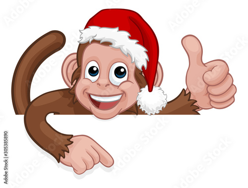 A Christmas monkey animal cartoon character in a Santa hat. Behind a sign peeking over a sign and pointing at it while giving a thumbs up