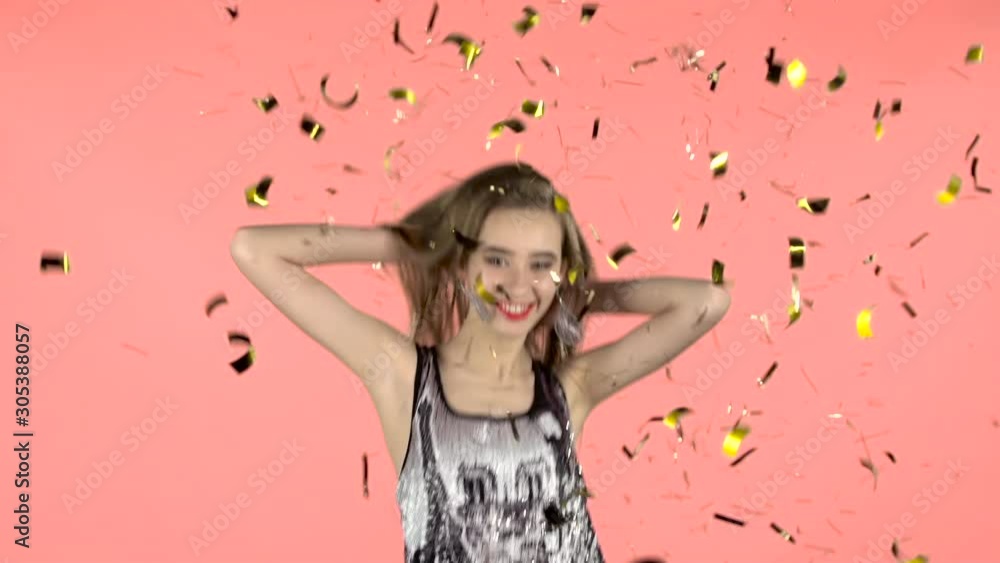 Girl posing with falling confetti in studio. Pink background. Slow motion Girl posing with falling confetti in studio. Pink background. Slow motion