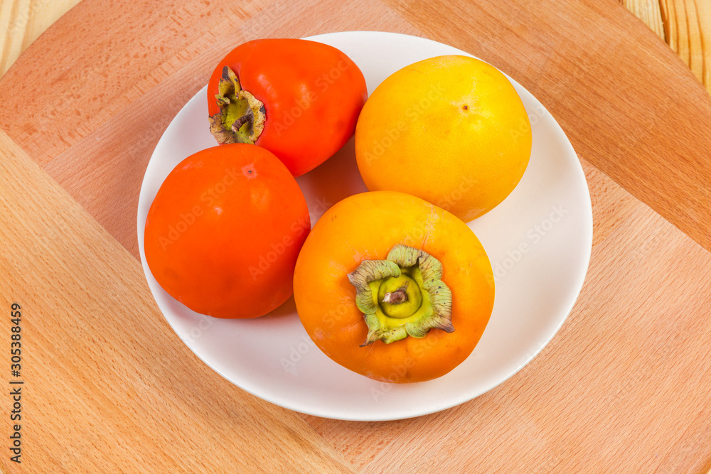 Different persimmon fruits on white dish on the wooden surface Different persimmon fruits on white dish on the wooden surface
