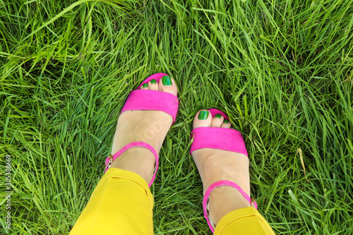 Pedicure in pink sandals with green nail Polish on the background of young grass in summer on the lawn.