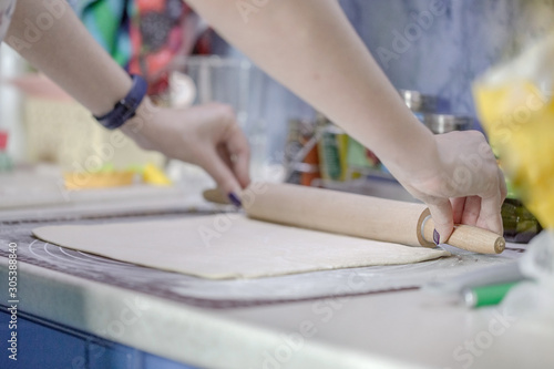 Woman rolls puff pastry with a wooden rolling pin on a silicone mat for dough. The process of cooking baking.