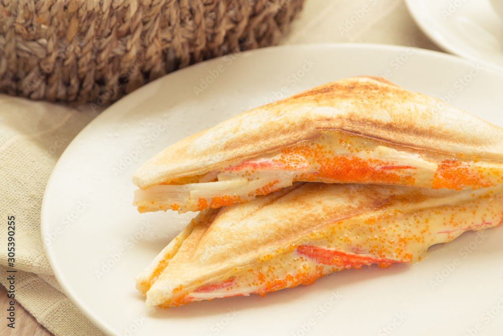 Sandwich stuffed with crab stick and shrimp eggs in white dish on wooden table.