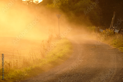 Clouds of dust in the air illuminated by the sunlight in counryside landscape with a gravel road after a tractor has driven along. Seen in Franconia / Bavaria in Germany near Haimendorf in September