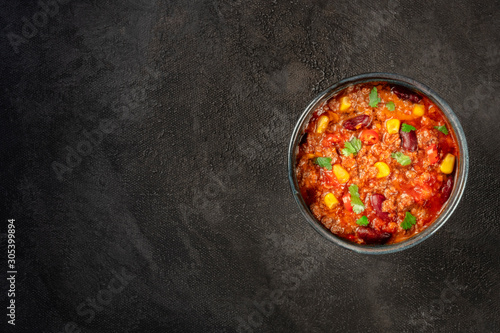 Chili con carne, Mexican stew with beans, ground meat, corn, and chilli peppers, overhead shot on a black background with copyspace