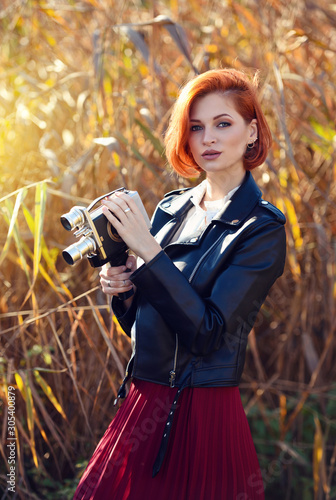 Beautiful young redhaired woman holds a video camera photo