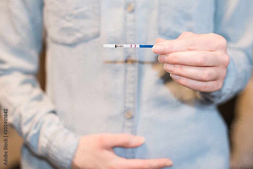 Schwangere Frau mit Schwangerschaftstest in der Hand und anderer Hand auf dem Babybauch Querformat Schwangere Frau mit Schwangerschaftstest in der Hand und anderer Hand auf dem Babybauch Querformat