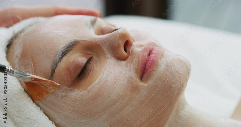 Close up of cosmetologist applies facial clay mask on an young beautiful woman face before ultrasonic cleaning procedure for skin pores and deep moisturizing. Close up of cosmetologist applies facial clay mask on an young beautiful woman face before ultrasonic cleaning procedure for skin pores and deep moisturizing.