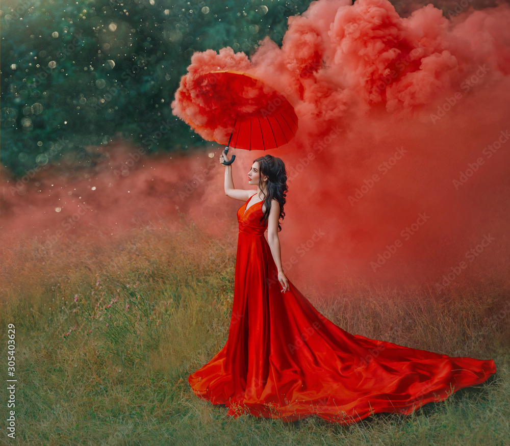 woman in red silk long dress train with umbrella. Art design photography.  Idea Creative photo shoot with colored smoke bomb. Magical light nature.  Glamorous fashion lady walks in woods. valentines day Stock