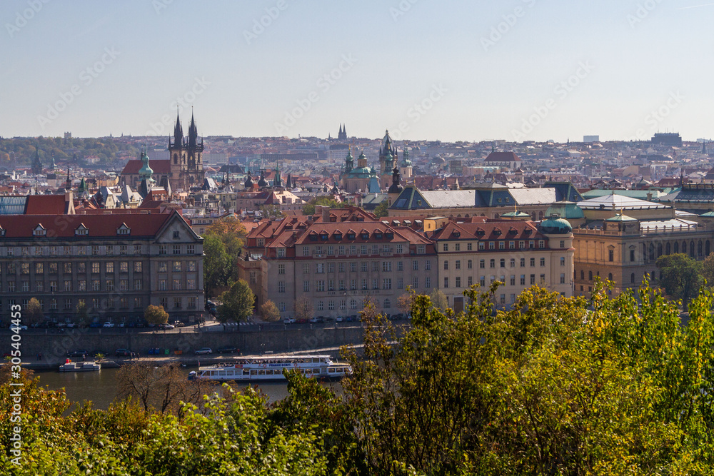 City views Prague autumn. Green foliage in the foreground. Tiled roofs. Vlatva river. Bridge. Boats. View from above.