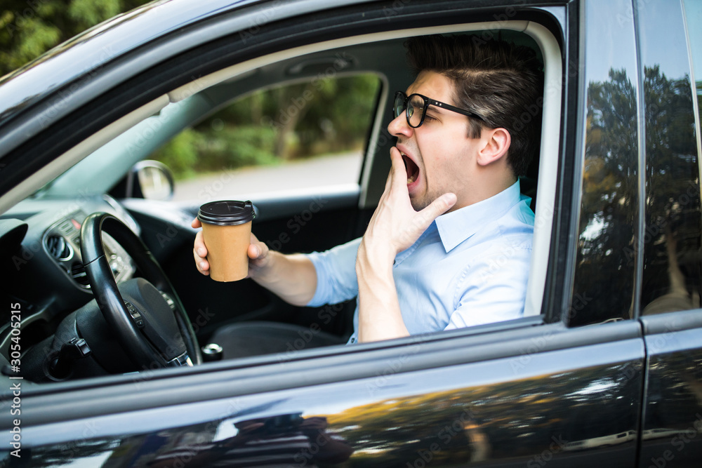 Young man drink coffee feeling tired and yawning while driving a car