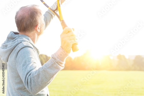 Senior man serving badminton in park on sunny day