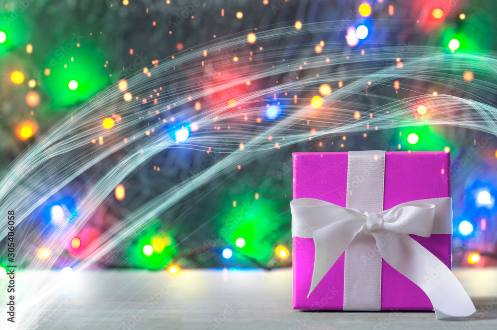 Purple gift box with white ribbon. In the background are garlands, bokeh and lights. Purple gift box with white ribbon. In the background are garlands, bokeh and lights.