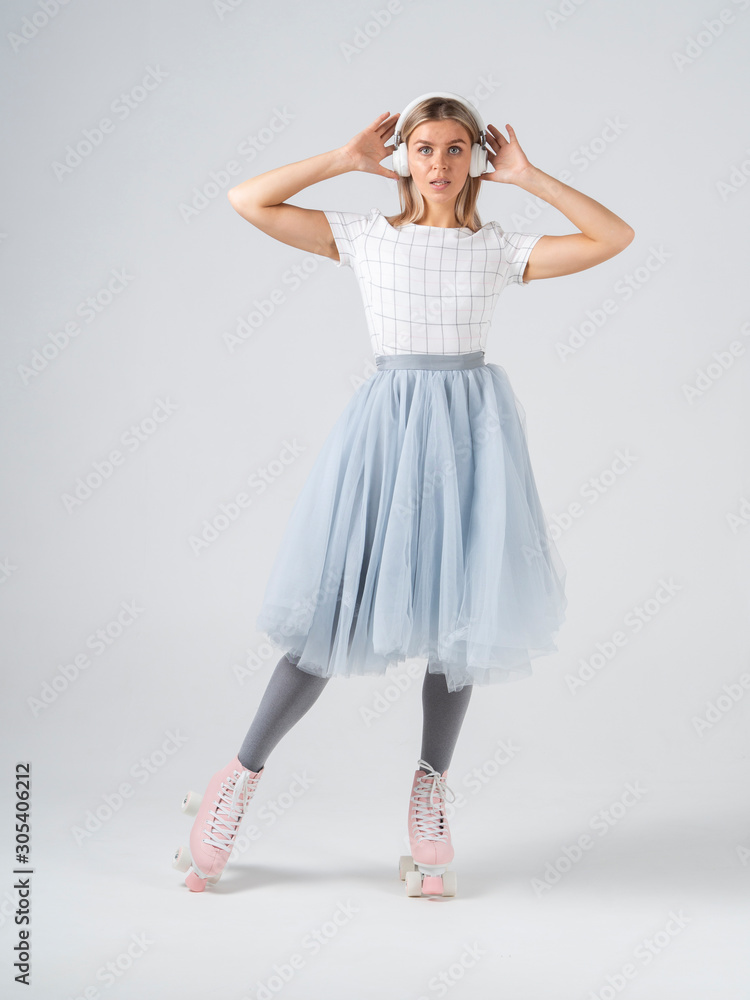 Naklejka premium A young woman in retro quad roller skates listening to music and holds headphones a white cyclorama background