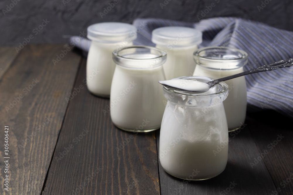 Natural homemade yogurt in glass jars with spoon on dark wooden background Natural homemade yogurt in glass jars with spoon on dark wooden background