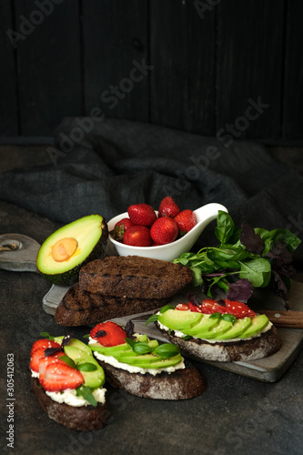 Toast or sandwich with avocado, cheese, strawberries, herbs and seeds on a dark background. An idea for bruschetta or for a healthy snack. Healthy vegan breakfast.