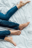 partial view of barefoot couple in denim jeans lying on bed