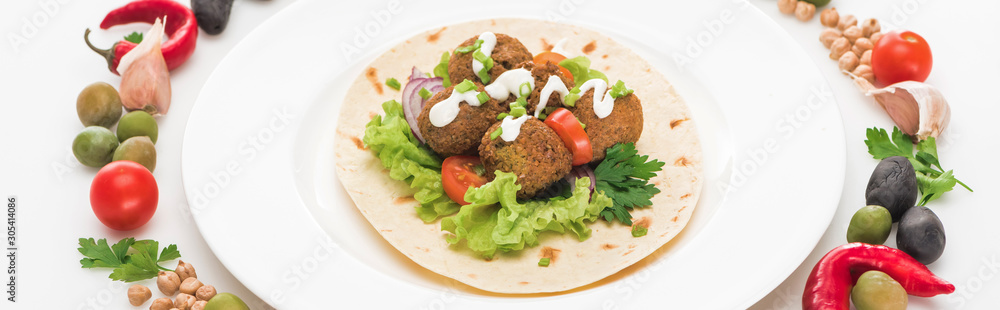 vegetables arranged in round frame around falafel on pita on plate on white background, panoramic shot