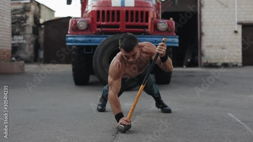 Muscular handsome sportsman doing push-ups with a sledgehammer in front of a fire engine photo