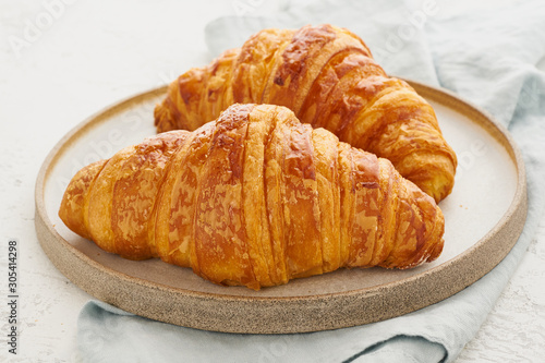 Two delicious croissants on plate and hot drink in mug. Morning French breakfast with fresh pastries. Light gray background.