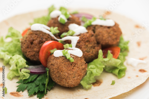close up view of fresh falafel balls on pita with vegetables and sauce on white background