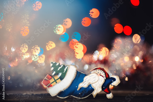 wooden santaklaus with gifts and Christmas tree on the bokeh lights background photo