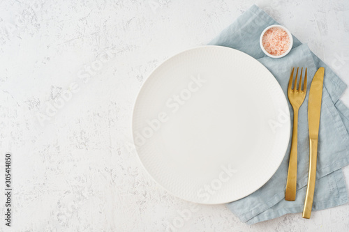 Clean empty white plate, fork and knife on white stone table, copy space, mock up, top view. Concept for menu