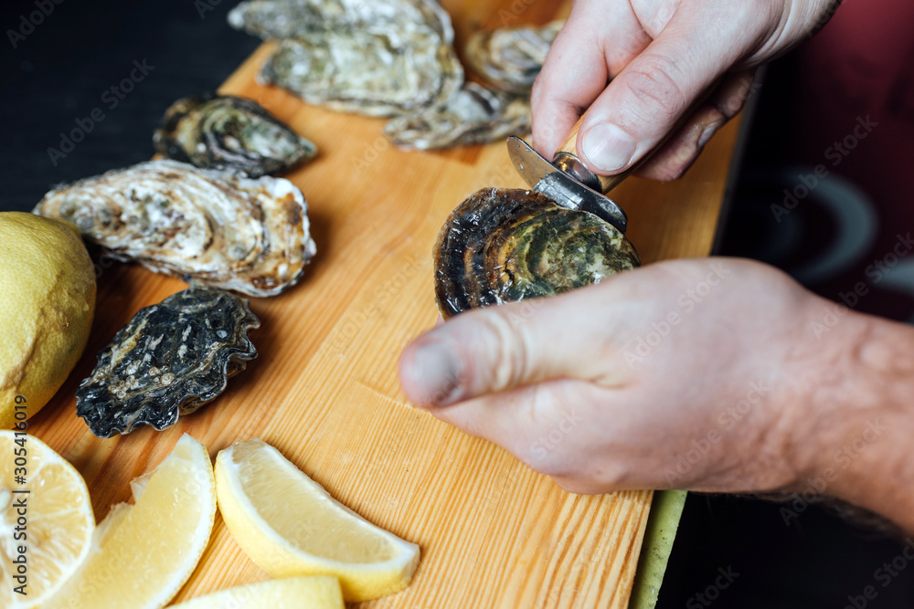 Process of shucking oysters with the knife for oysters in the restaurant, focus on the male hands