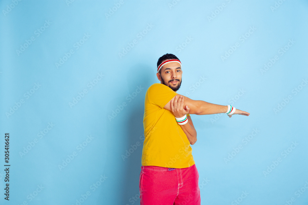 Young caucasian man in bright clothes training on blue background Concept of sport, human emotions, facial expression, healthy lifestyle, youth, sales. Doing stretching exercises. Copyspace. Young caucasian man in bright clothes training on blue background Concept of sport, human emotions, facial expression, healthy lifestyle, youth, sales. Doing stretching exercises. Copyspace.
