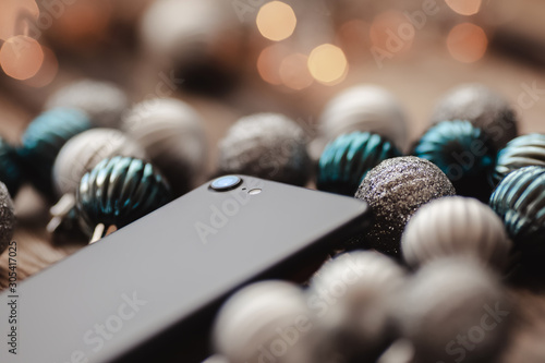 Black smartphone with camera on wooden background with Christmas balls and bokeh light photo