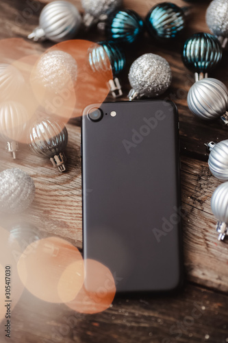 Black smartphone with camera on wooden background with Christmas balls and bokeh light photo