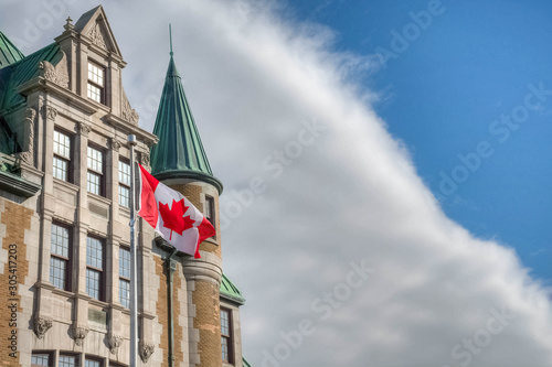 Canadian flag in the wind, beside historic building.