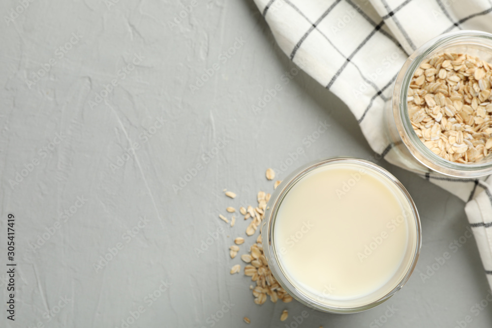 Glass of oat milk, oatmeal seeds, napkin on grey background, space for text. Top view Glass of oat milk, oatmeal seeds, napkin on grey background, space for text. Top view