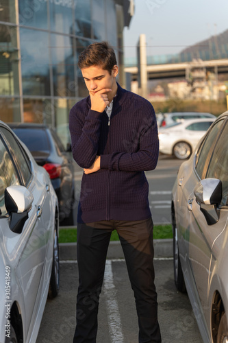 Tableau sur toile A young man stands and thinks about choosing between two second-hand car at a car showroom