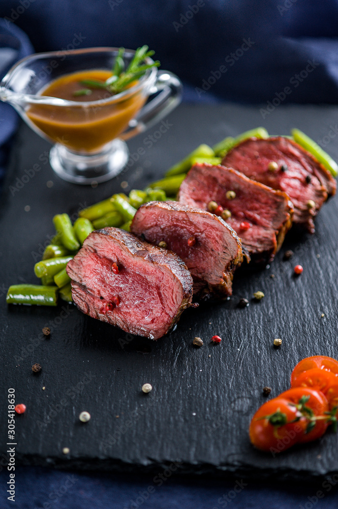 Steak medallion with vegetables and sauce on a black plate with coals