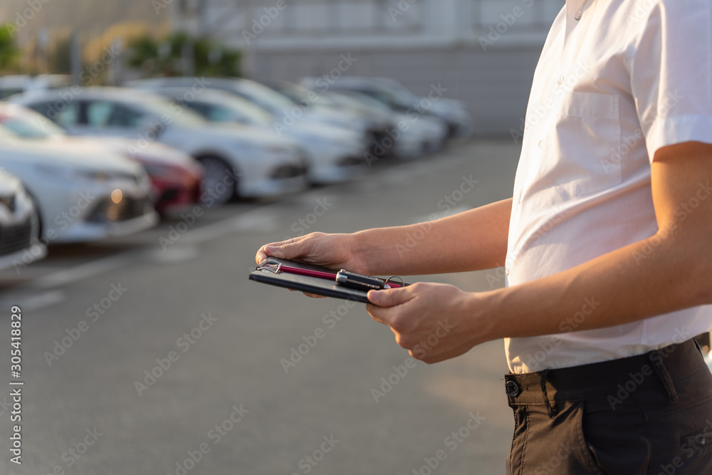 Sales manager with clipboard and key of car, On the background of the auto park. Dealership of rent, hire cars.