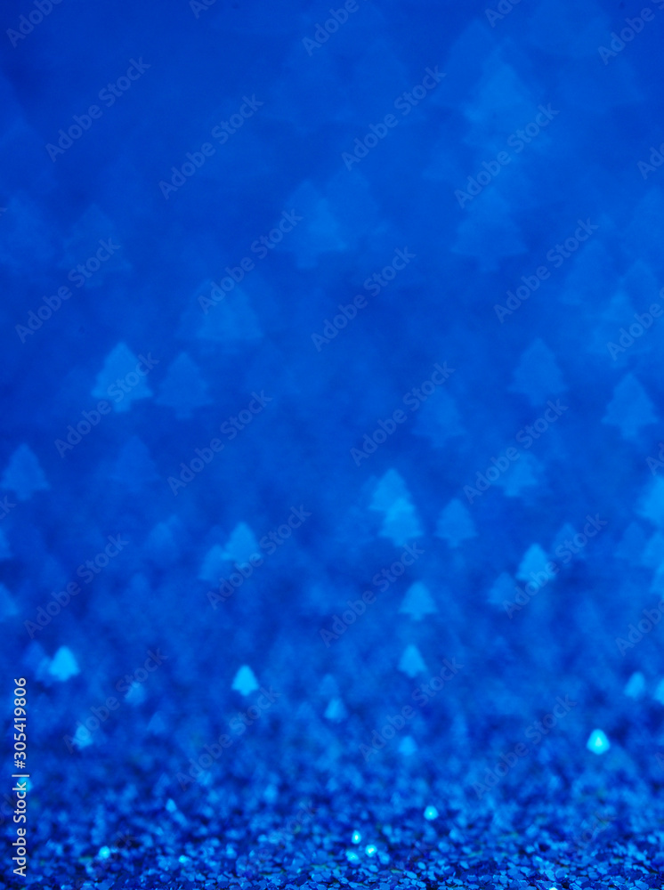 Blue holiday glitter background with Christmas tree bokeh.