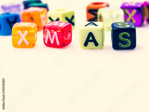 Closeup  macro photography of multicolored small plastic alphabet dice of Xmas word on white cross processed color tone background for holidays anniversary  celebration greeting card concept a