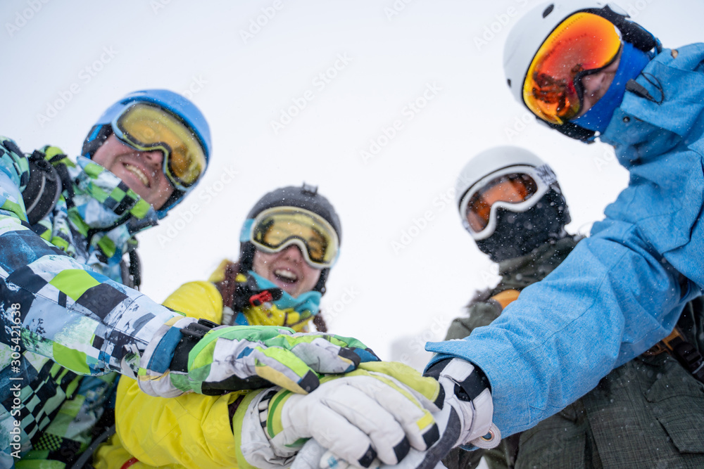 Photo from bottom of four happy snowboarders in helmet doing handshake on blue sky. Photo from bottom of four happy snowboarders in helmet doing handshake on blue sky.