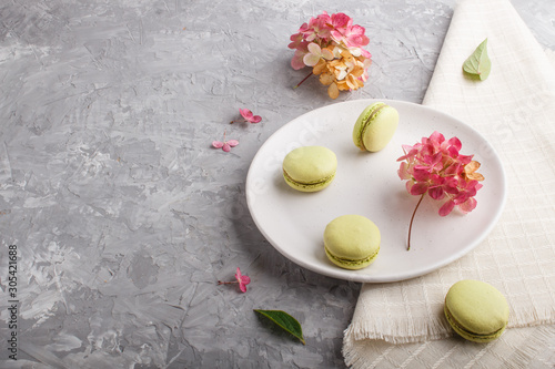 Green macarons or macaroons cakes on white ceramic plate on a gray concrete background side view.