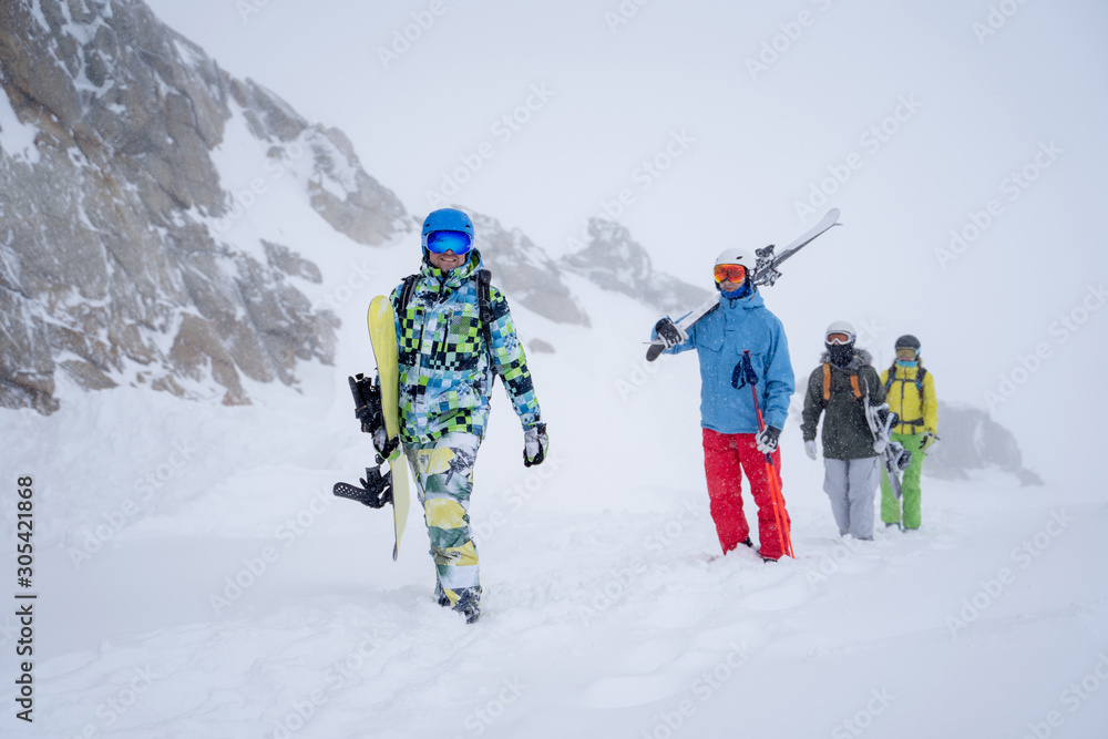 Photo of four sports people with skis and snowboard walking in winter resort